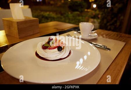 Torta Pavlova con fragole fresche, mirtilli e foglie di menta su un piatto di ceramica bianca sul tavolo da restauro. Meringa dessert, foto da vicino Foto Stock