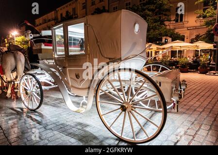 Cracovia, Polonia - 29 agosto 2018: Carrozza con cavalli che trasportano turisti di notte sulla piazza principale del mercato o Rynek Głowny, strada dello shopping con resto Foto Stock