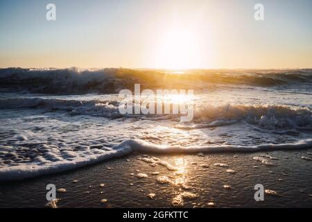 onde che si infrangono sulla riva della spiaggia con schiuma al tramonto Foto Stock