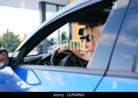 Donna sicura e bella in occhiali da sole. Vista posteriore di una giovane donna attraente in un abbigliamento casual alla guida di un'auto Foto Stock