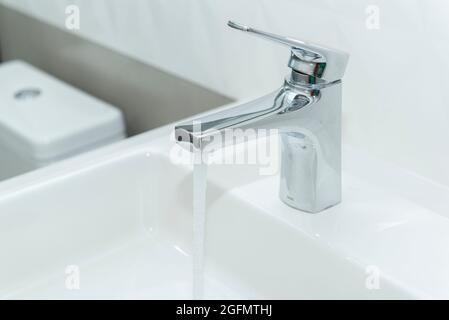 Lavello rettangolare in marmo bianco con moderno bacino overlay e rubinetto in acciaio inossidabile lucido. Aprire l'acqua di sgushing del rubinetto. Foto Stock