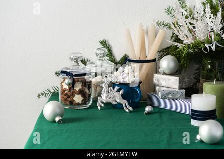 Tavolo natalizio o di Capodanno decorato per le feste, thuja e rami decorativi di abete rosso, candele e palle grigie, biscotti in un vaso Foto Stock