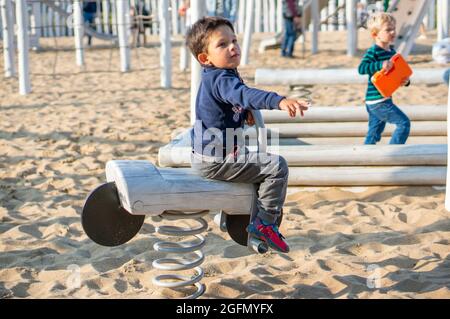 POZNAN, POLONIA - 26 ago 2018: Un bambino che indossa un maglione blu seduto su attrezzature di legno swing sulla sabbia in un parco giochi Foto Stock