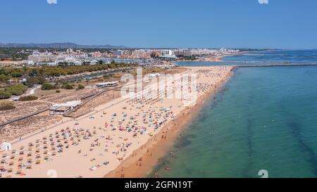 Vista aerea della lussuosa spiaggia di Falesia a Vilamoura. Con i turisti che prendono il sole sui lettini. Porto di Marina con yacht, sullo sfondo. Foto Stock