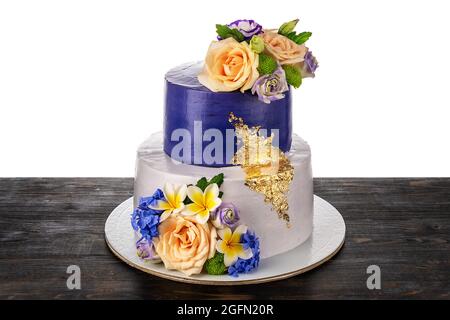 Una bella torta nuziale concettuale fatta di due piani, fiori di rosa, e gioielli d'oro. Su un tavolo di legno, su sfondo bianco. Foto Stock
