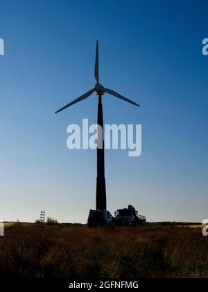 Turbina eolica al tramonto con veicoli sotto, Cornovaglia, Regno Unito Foto Stock