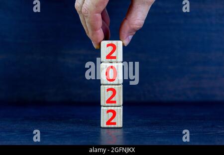 2022 felice anno nuovo simbolo. I cubi di legno simboleggiano il cambiamento dal 2021 al nuovo anno 2022. Mano dell'uomo d'affari. Bellissimo sfondo nero. Spazio di copia Foto Stock