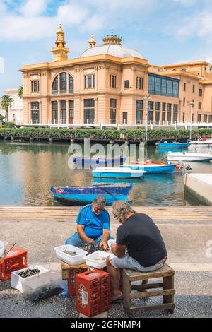 I pescatori locali lavano, puliscono e vendono frutta fresca di mare pronta a mangiare in un mercato di Street food all'aperto sul lungomare di Bari, Puglia, verticale Foto Stock