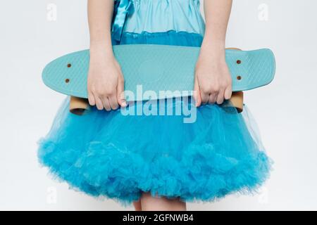 Primo piano ragazza adolescente che indossa gonna blu soffici che tiene in mano mani un bordo blu del penny su sfondo bianco Foto Stock
