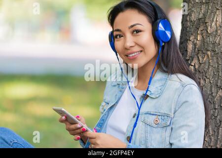 Primo piano ritratto di donna asiatica in cuffie con smartphone. Sorride e ascolta la sua musica preferita o la sua lezione educativa. Foto Stock