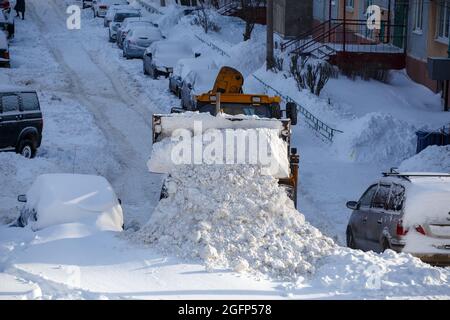 trattore che rimuove la neve dal parcheggio vicino a un edificio residenziale durante la giornata invernale Foto Stock