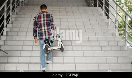 Uno studente sale le scale per l'università con uno scooter elettrico. Concetto di città moderna. Stile di vita tecnologico ecologico. Foto Stock