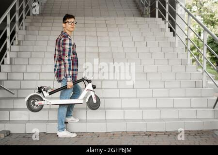 Uno studente sale le scale per l'università con uno scooter elettrico. Concetto di città moderna. Stile di vita tecnologico ecologico. Foto Stock