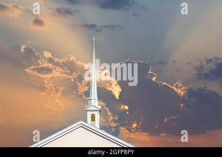 Alto campanile di chiesa bianca con croce sulla cima aganista un cielo arancione con raggi solari a Punta Gorda Florida Foto Stock