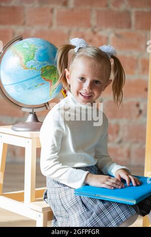 Ritratto di scolaretta caucasica seduta di fronte al globo in classe Foto Stock