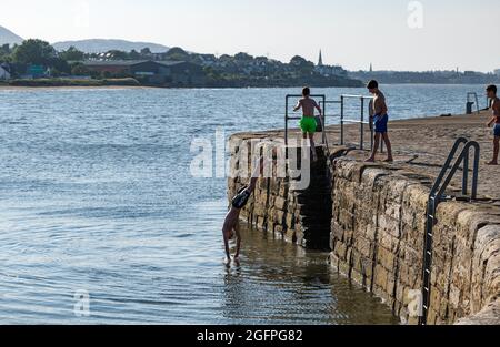 Musselburgh, East Lothian, Scozia, Regno Unito, 26 agosto 2021. UK Meteo: Giornata di sole per rinfrescarsi in mare. I bambini saltano fuori dalla parete del porto nel Firth of Forth durante il tempo caldo Foto Stock