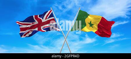 Bandiere di gran Bretagna e Senegal ondeggiavano nel vento su flagpoli contro il cielo con le nuvole in giorno di sole. Simbolizzazione della relazione, dialogo tra due Foto Stock