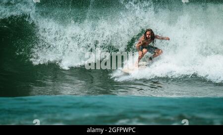 Un uomo locale dai capelli lunghi che naviga giù un'onda di spruzzi alla costa pacifica del Costa Rica, America centrale Foto Stock