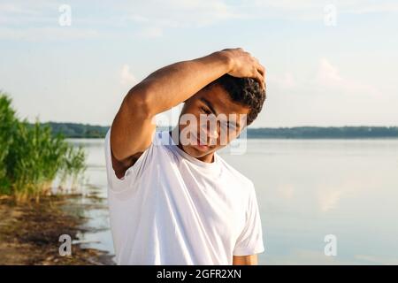 Uomo afroamericano in maglietta bianca che posa sulla riva del fiume Foto Stock