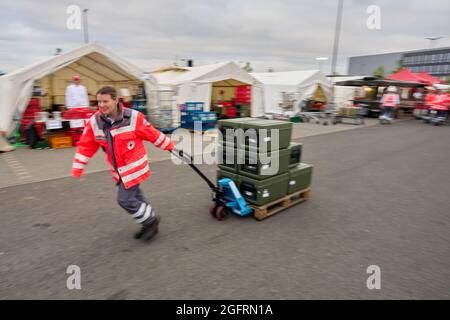 Grafschaft, Germania. 23 Agosto 2021. Un assistente del centro di ristorazione tedesco della Croce Rossa porta il cibo in contenitori termici ai veicoli che guidano verso i punti di distribuzione. Qui, più di 10000 pasti sono preparati tre volte al giorno per le vittime del disastro alluvionale dell'Ahr e per i numerosi aiutanti. Credit: Thomas Frey/dpa/Alamy Live News Foto Stock