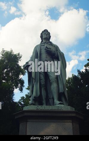 FRANCOFORTE, GERMANIA - 20 agosto 2021: Monumento di Friedrich Schiller nella zona del parco di Taunusanlage a Francoforte. Retroilluminazione contro un cielo blu nuvoloso. Crea Foto Stock