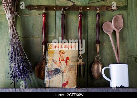 vecchio libro di cucina con utensili da cucina di fronte al muro di legno verde Foto Stock