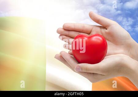 Le mani del bambino tengono un cuore sullo sfondo della bandiera dell'Irlanda, concetto di assistenza sanitaria. Foto Stock