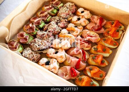 Scatola con piccoli sandwich, bruschetta con salumi, formaggi e frutti di mare. Snack gourmet in cartone per catering a buffet per feste. Foto Stock