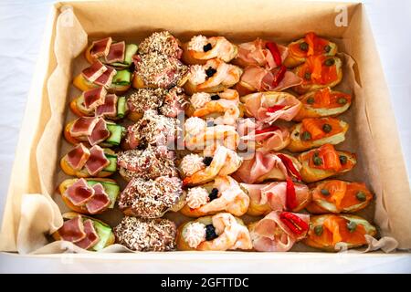 Scatola con piccoli sandwich, bruschetta con salumi, formaggi e frutti di mare. Snack gourmet in cartone per catering a buffet per feste. Foto Stock