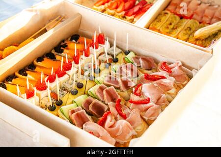 Spuntini gourmet in cartone con sandwich, eclarie, bruschetta con salumi, formaggi e frutti di mare per catering a buffet e feste. Foto Stock