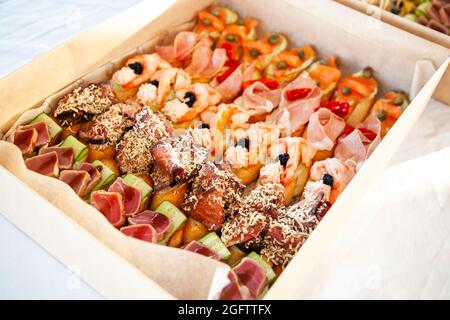 Scatola con piccoli sandwich, bruschetta con salumi, formaggi e frutti di mare. Snack gourmet in cartone per catering a buffet per feste. Foto Stock