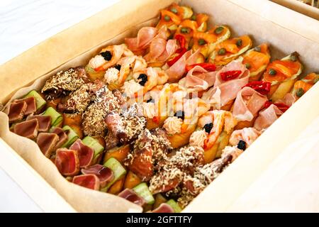 Scatola con piccoli sandwich, bruschetta con salumi, formaggi e frutti di mare. Snack gourmet in cartone per catering a buffet per feste. Foto Stock