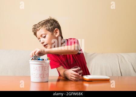 Un bambino che rimuove una batteria scarica da un giocattolo e la inserisce in un cestino per il riciclaggio. Concetto di educazione dei bambini ai valori ambientali. Foto Stock