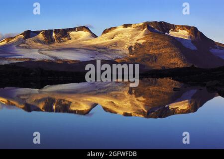 Luce di mattina presto sulle cime di Fannaraken con un riflesso simile a uno specchio in un lago glaciale, Norvegia, Parco Nazionale di Jotunheimen, Fannaraken Foto Stock