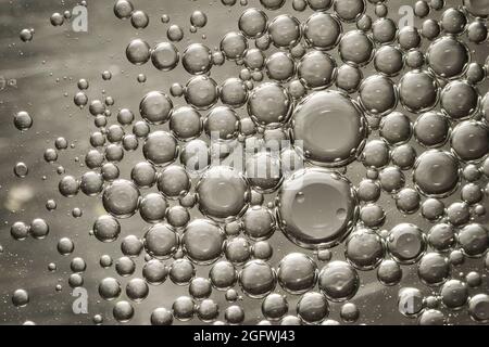 Bolle d'olio in acqua che fanno un interessante macro modello grigio acciaio Foto Stock