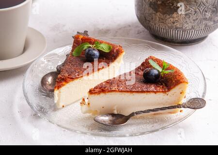 Fetta di cheesecake basca bruciata in casa su un piatto con mirtilli e foglie di menta su sfondo chiaro. Foto Stock