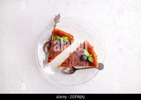 Fetta di cheesecake basca bruciata in casa su un piatto con mirtilli e foglie di menta su sfondo chiaro. Foto Stock