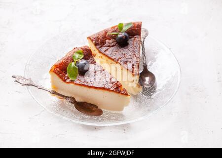 Fetta di cheesecake basca bruciata in casa su un piatto con mirtilli e foglie di menta su sfondo chiaro. Foto Stock