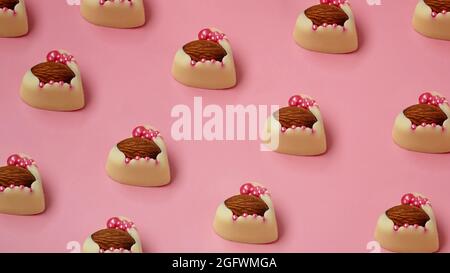 Caramelle al cioccolato bianco con mandorle in fila. Dolci a forma di cuore. Dolci fatti a mano su sfondo rosa Foto Stock