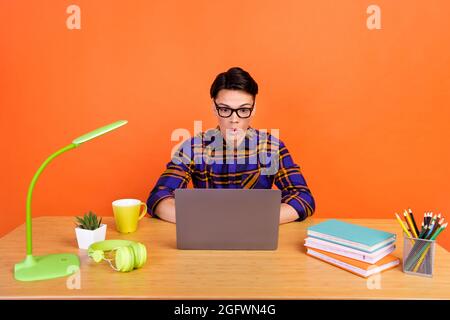 Foto di impressionato scioccato uomo vestito a scacchi vetri seduta tavolo tipizzazione moderno dispositivo isolato colore arancione sfondo Foto Stock