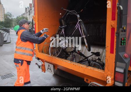 Hannover, Germania. 27 ago 2021. Timo Clever, dipendente dell'aha Zweckverband Abfallwirtschaft Region Hannover, lancia una vecchia bicicletta su un camion per rifiuti. L'azienda aha sta rimovendo ancora una volta le cosiddette "bici a schiaffo" che si trovano da mesi sugli angoli della strada e che ovviamente non vengono più utilizzate. Credit: Julian Stratenschulte/dpa/Alamy Live News Foto Stock