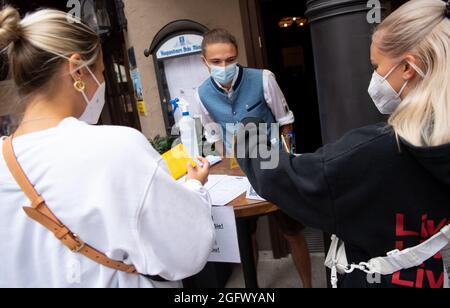 27 agosto 2021, Baviera, Monaco: Un dipendente di un pub controlla la prova 3G di due ospiti all'ingresso. Gli ospiti del ristorante devono essere vaccinati, sottoposti a test o recuperati quando soggiornano all'interno. Foto: Sven Hoppe/dpa Foto Stock