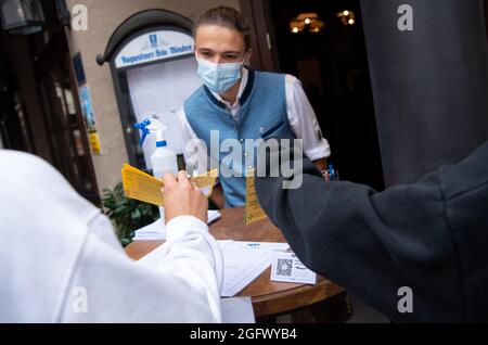 27 agosto 2021, Baviera, Monaco: Un dipendente di un pub controlla la prova 3G di due ospiti all'ingresso. Gli ospiti del ristorante devono essere vaccinati, sottoposti a test o recuperati quando soggiornano all'interno. Foto: Sven Hoppe/dpa Foto Stock
