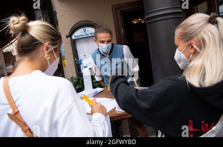 27 agosto 2021, Baviera, Monaco: Un dipendente di un pub controlla la prova 3G di due ospiti all'ingresso. Gli ospiti del ristorante devono essere vaccinati, sottoposti a test o recuperati quando soggiornano all'interno. Foto: Sven Hoppe/dpa Foto Stock