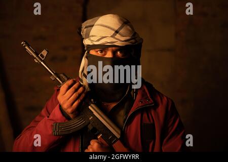 Ritratto di arrabbiato militante islamico o soldato con la copertura facciale tenendo la pistola guardando la macchina fotografica Foto Stock