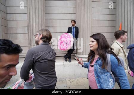 La gente cammina davanti a un dimostratore durante una protesta da parte dei membri della ribellione di estinzione alla Banca d'Inghilterra, nella città di Londra. Data foto: Venerdì 27 agosto 2021. Foto Stock