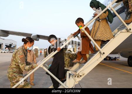 Sigonella, Italia. 26 agosto 2021. Un membro del servizio degli Stati Uniti assiste una famiglia afghana evacuata da Kabul all'arrivo alla Stazione aeronavale di Sigonella il 26 agosto 2021 a Sigonella, Italia. NAS Sigonella fornisce alloggio temporaneo per gli evacuati dall'Afghanistan come parte dell'operazione Rifugi Alleati. Credit: Planetpix/Alamy Live News Foto Stock