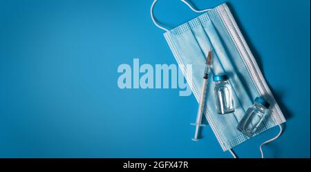 vaccinazione - flaconcini di vaccino con siringa e maschera medica su sfondo blu. spazio per la copia del banner Foto Stock