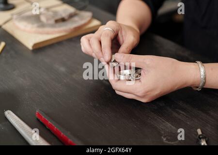 Mani di gioielliere che controlla anelli d'argento mentre lo fanno nella propria officina Foto Stock
