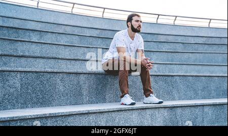 Uomo solitario sui gradini. Il ragazzo calmo in stile casual siede pensivo Foto Stock